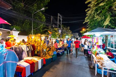 Chiang Mai, Tayland - 3.11.2019: Günbatımından kısa bir süre sonra Chiang Mai şehrinde gece pazarı. Turistler yolda yürüyorlar. Yandaki tezgahta Taylandlı satıcılar var. Hatıralar ve sokak yemekleri, yaz günü.