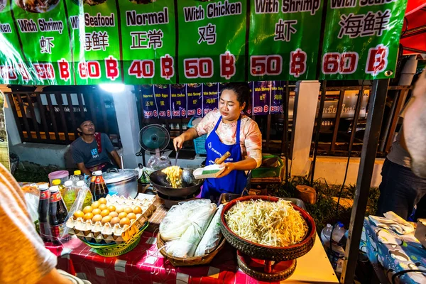 CHIANG MAI, TAILANDIA - 3.11.2019: Las mujeres preparan comida callejera en el mercado nocturno de la ciudad de Chiang Mai. Famosa comida tailandesa llamada Pad Thai ordenada por el turista. Huevos, fideos y verduras frescas —  Fotos de Stock