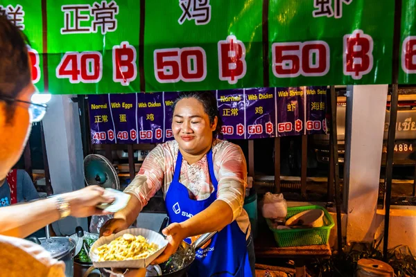CHIANG MAI, TAILANDIA - 3.11.2019: Las mujeres preparan comida callejera en el mercado nocturno de la ciudad de Chiang Mai. Famosa comida tailandesa llamada Pad Thai ordenada por el turista. Huevos, fideos y verduras frescas —  Fotos de Stock