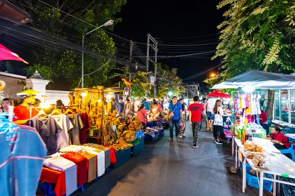 Chiang Mai, Tayland - 3.11.2019: Günbatımından kısa bir süre sonra Chiang Mai şehrinde gece pazarı. Turistler yolda yürüyorlar. Yandaki tezgahta Taylandlı satıcılar var. Hatıralar ve sokak yemekleri, yaz günü.