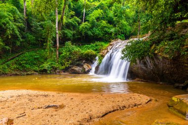 Beautiful waterfall Mae Sa, Thailand. Fresh and pure water stream is flowing on the rock stone ground in tropical rainforest. Fresh plants and trees above river. Vibrant colors in pure nature