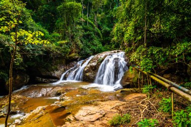 Beautiful waterfall Mae Sa, Thailand. Fresh and pure water stream is flowing on the rock stone ground in tropical rainforest. Fresh plants and trees above river. Vibrant colors in pure nature