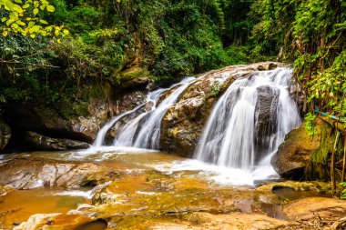 Beautiful waterfall Mae Sa, Thailand. Fresh and pure water stream is flowing on the rock stone ground in tropical rainforest. Fresh plants and trees above river. Vibrant colors in pure nature