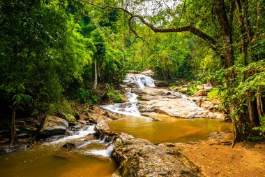 Beautiful waterfall Mae Sa, Thailand. Fresh and pure water stream is flowing on the rock stone ground in tropical rainforest. Fresh plants and trees above river. Vibrant colors in pure nature