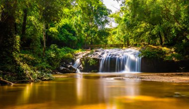 Beautiful waterfall Mae Sa, Thailand. Fresh and pure water stream is flowing on the rock stone ground in tropical rainforest. Fresh plants and trees above river. Vibrant colors in pure nature