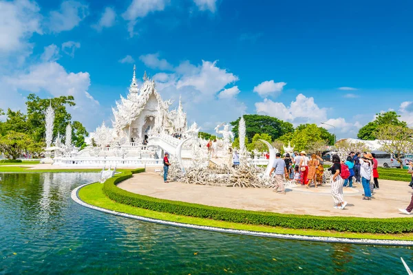 Chiang Rai, Tayland - 6.11.2019: Chiang Rai şehri yakınlarındaki ünlü beyaz tapınağı (Wat Rong Khun) ziyaret eden turistler. Cennete giden yol, günahkarların lanetli ruhlarının üzerinde köprü olan beyaz tapınak. Mavi gökyüzü.