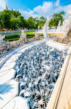 Tayland 'ın Chiang Rai şehrindeki Beyaz Tapınak (Wat Rong Khun). Cennete giden yolu, günahkarların lanetlenmiş ruhları üzerinde köprüsü olan güzel Budist antik binası. Ünlü turist merkezi. Mavi gökyüzü.