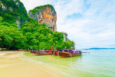 Tayland, Krabi 'deki ünlü Railay plajı. Uzun kuyruklu tekneler kireçtaşı kayasının yakınındaki yolcular için hazırdır. Tropik cennet, ünlü turistik mekan. Turkuaz deniz beyaz kumla.