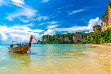 Tayland 'ın Krabi kasabasındaki ünlü Railay plajında tek başına uzun kuyruklu bir tekne. Tipik Tayland tatili görüntüsü. Saf deniz, beyaz kum ve mavi gökyüzü olan tropik bir cennet. Arka planda büyük kayalar