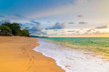 Tayland 'daki Koh Lanta adasındaki tropik plaj manzarası. Sahildeki bar güzel günbatımında turistler için hazırlanır. Yumuşak ışık, canlı renkler. Gökyüzü bulutlu sakin denizin üstünde.