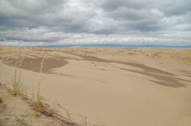 Sabahları kum tepelerinin üzerinde dramatik bulutlar. Dorgon Tuzlu Su Gölü kıyısında Barkhan Moğol-Els kumları. Doğa ve seyahat. Moğolistan, Gobi Çölü, Govi-Altai