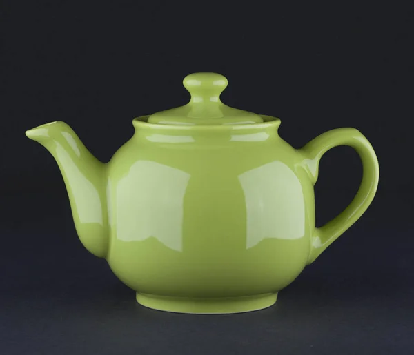Green ceramic teapot isolated on black background
