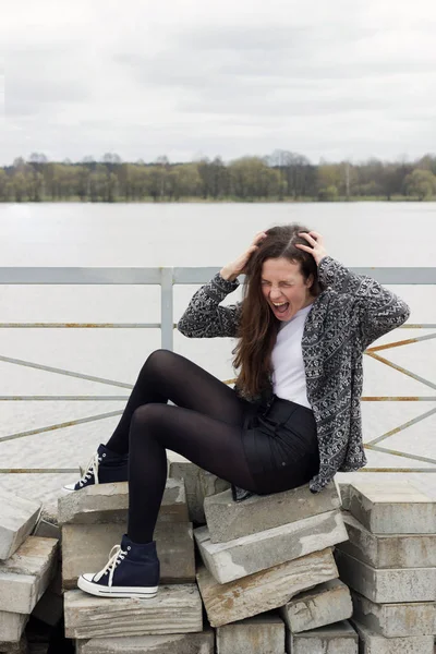Кричащая девушка, сидящая на бетонных блоках возле реки — стоковое фото