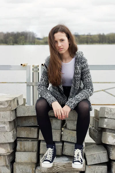 Chica sentada en bloques de hormigón cerca del río — Foto de Stock
