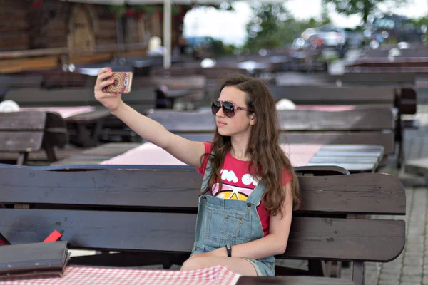 Young girl doing selfie in sunglasses on the terrace of a cafe — Stock Photo, Image
