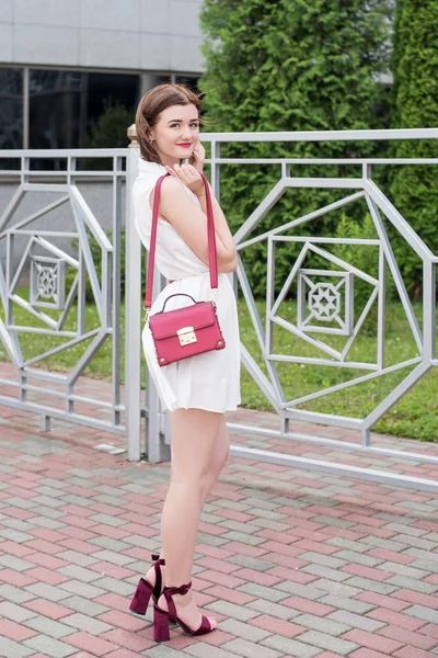 Chica joven en un vestido blanco con un bolso rojo caminando por la ciudad — Foto de Stock