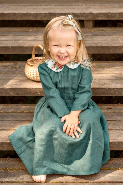 vintage retro tarzı keten, küçük kız elbise yalınayak oturan ve bir ahşap merdiven Park hasır sepet ile gülüyor