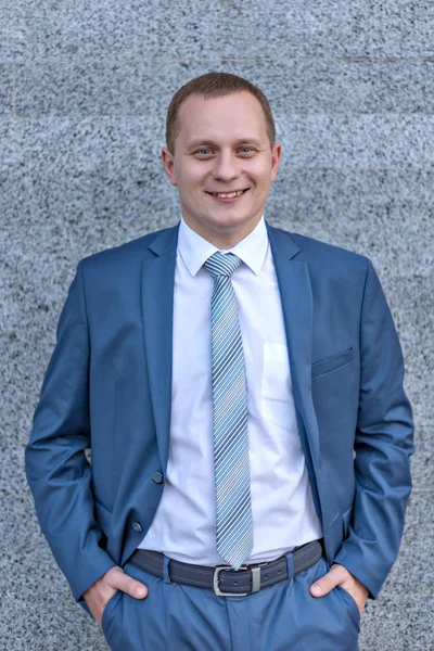 Portrait of a young serious smiling businessman in grey blue suit — Stock Photo, Image