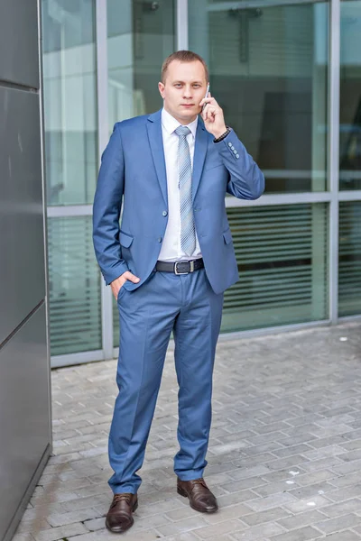 Portrait of a young serious businessman in blue suit talking holding phone — Stock Photo, Image