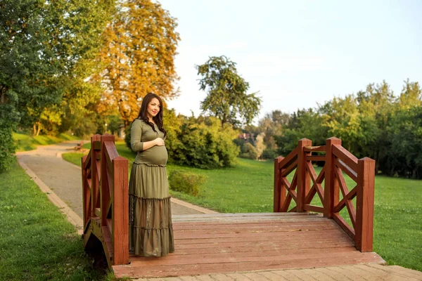 Молодая беременная женщина в ожидании ребенка, стоящего в парке под солнечными лучами — стоковое фото
