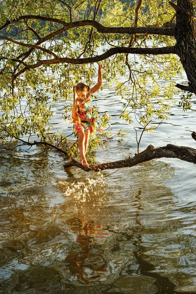 Молода дівчина стоїть на гілці дерева над водою річки і бризкає ногу — стокове фото