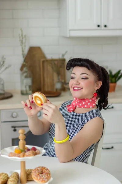 Alfiler chica emocionalmente comiendo un donut y riendo en la cocina en la mesa — Foto de Stock