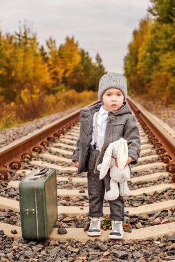 bir terk edilmiş tren rayları üzerinde ormanın ortasında bir tavşan yanındaki eski moda bir bavul vintage giysiler içinde kaybolmuş küçük bir çocuk hugs