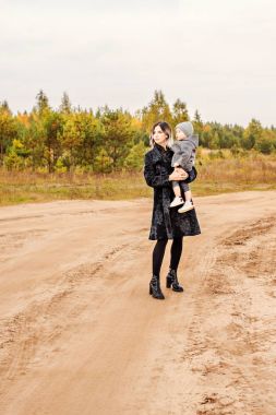 Anne kucağında oğluyla tozlu kumlu kırsal yolda gidiyor