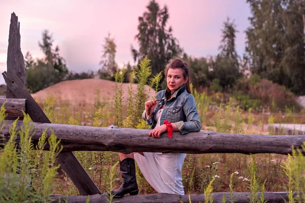 a young cowgirl at sunset near a rustic wooden fence