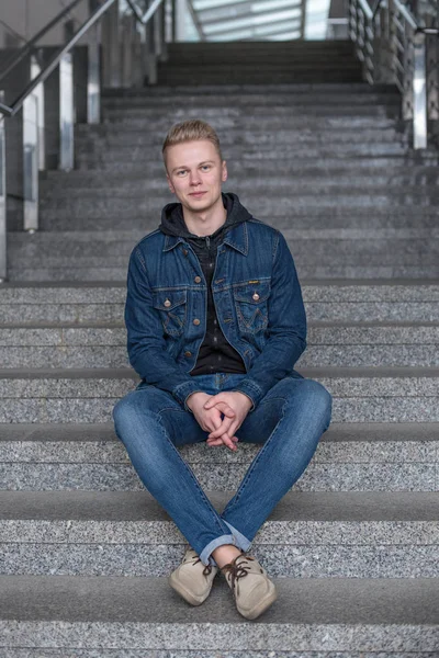 Fellow is sitting on stairs in jeans and jeans jacket — Stock Photo, Image