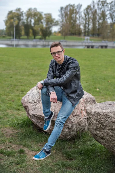 Student in black leather jacket sitting on a stone in the university backyard — Stock Photo, Image