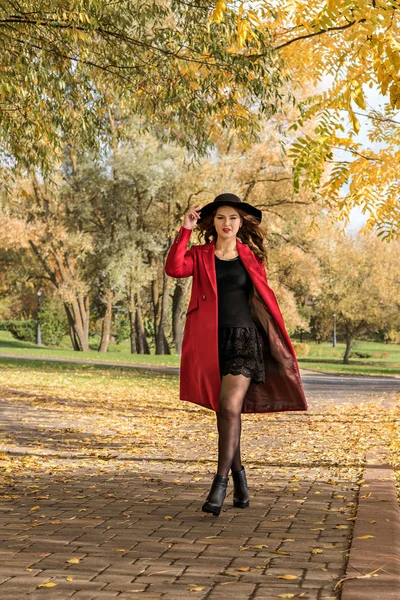 Девушка в красном пальто и шляпе, идущая по тропинке в осеннем парке — стоковое фото