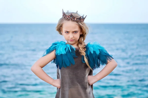 stern little princess girl in the crown watch frowningly, stands akimbo