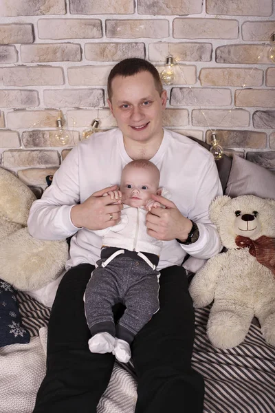 Портрет молодого батька з маленьким сином на руках посміхаючись сидячи на підлозі в домашньому затишному одязі — стокове фото