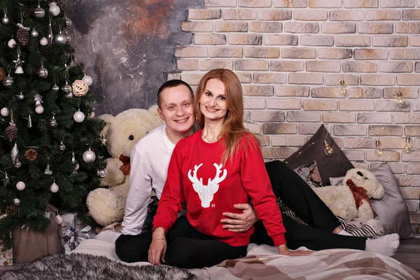 Close portrait of a young hugging couple in cozy Christmas clothes near the New Year tree — Stok fotoğraf