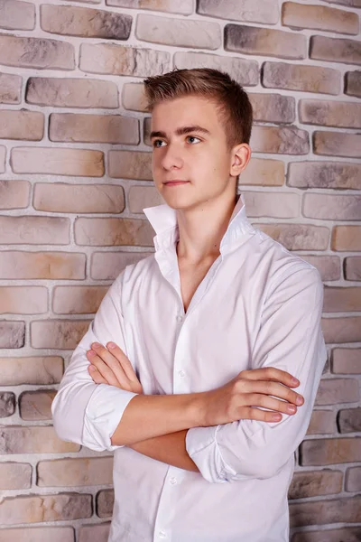 Close portrait of a male teenager model in a white shirt near a brick wall in a studio — Stock Photo, Image