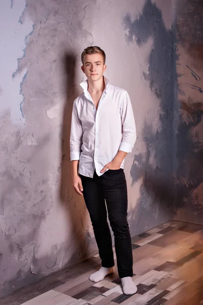 Νεαρός έφηβος με λευκό πουκάμισο και μαύρο τζιν στέκεται κοντά στον τοίχο και ένα χέρι στην τσέπη του Royalty Free Φωτογραφίες Αρχείου