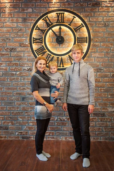 Сім'я жінка і брати і сестри підліток і малюк стоять в приміщенні біля величезного годинника за 5 хвилин до півночі Різдва — стокове фото
