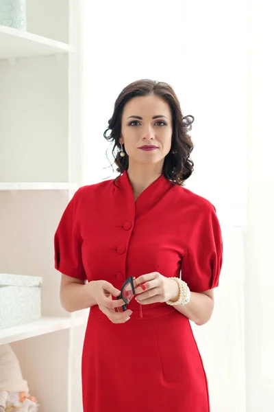 Портрет молодой серьезной брюнетки бизнес женщина стоит и держа очки в руках в красном платье — стоковое фото