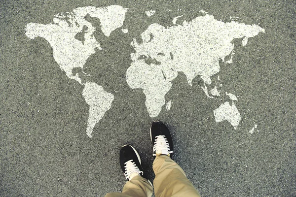 Карта мира на асфальтовой дороге. Вид сверху на ноги и обувь. POV — стоковое фото