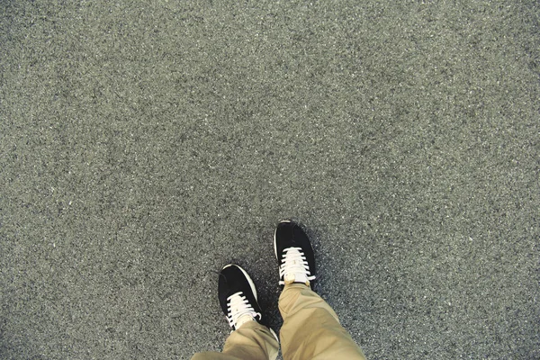 Ovanifrån i benen och skorna stående på asfaltvägen. Att göra beslut vad till gör nästa. minimalistisk stil — Stockfoto