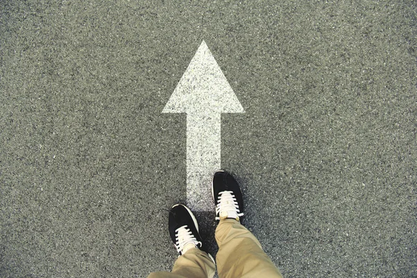 Forward arrow painted on an asphalt road. Top view of the legs and shoes. POV — Stock Photo, Image