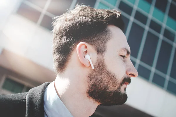 Close-up retrato de um homem barbudo com modernos fones de ouvido sem fio bluetooth — Fotografia de Stock