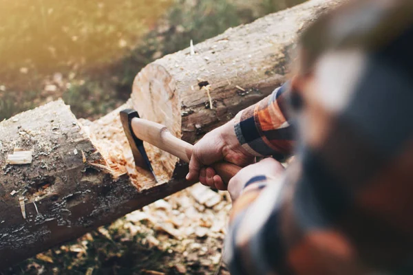 Sterke houthakker in een plaid shirt hakken van een logboek met een scherpe bijl in het bos — Stockfoto