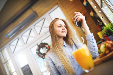 Büyük pencereler parlak samimi kafede yakınındaki bir masada otururken bir akıllı telefon arayan genç zarif kadın