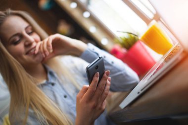 Güzel mutlu kız bir şey pencerenin modern café bir masada otururken bir smartphone üzerinde yazıyor. Smartphone portre