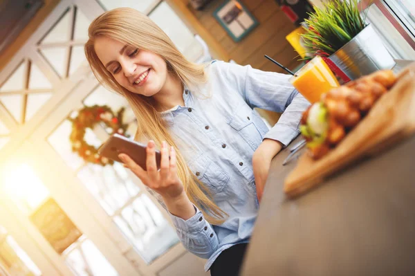 Feliz hermosa mujer comprueba las noticias en las redes sociales en un acogedor café de Navidad al estilo de la Provenza — Foto de Stock