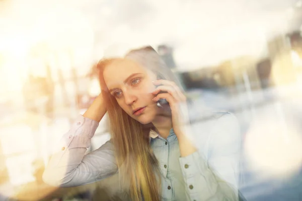 Nadenkend en mooie meisje praten aan de telefoon over iets in een café — Stockfoto