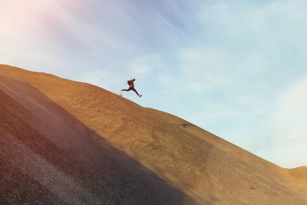 Brave man with backpack running and jumping on a dune in the desert — Stock Photo, Image