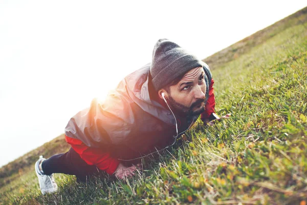 Bearded athlete in headphones warming up on a lawn